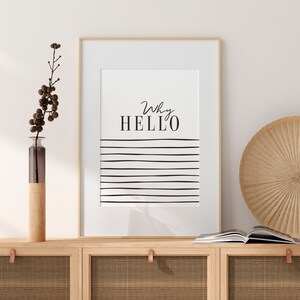 May include: A framed print with the text "Why Hello" in black script font on a white background. The print features a series of black horizontal lines below the text.