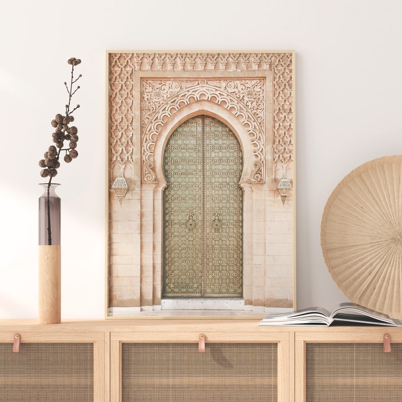 May include: A photograph of a decorative archway with an ornate door. The archway is made of stone and has intricate carvings. The door is made of wood and has a metal design. The photograph is in a light brown frame.