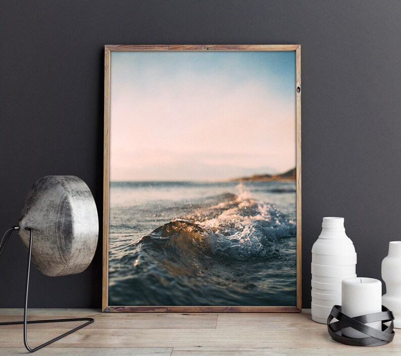 May include: A framed photograph of a wave breaking on a beach at sunset. The water is a deep blue and the sky is a soft pink and orange.