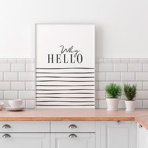 May include: A white framed print with black text that reads "Why HELLO" and black horizontal lines on a white background. The print is hanging on a white tiled wall above a wooden countertop and white cabinets.