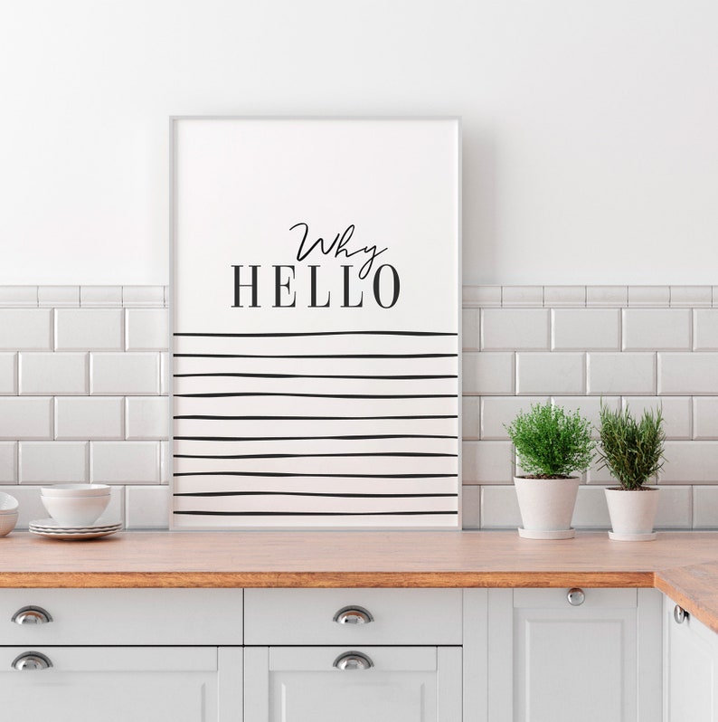 May include: A white framed print with black text that reads "Why HELLO" and black horizontal lines on a white background. The print is hanging on a white tiled wall above a wooden countertop and white cabinets.