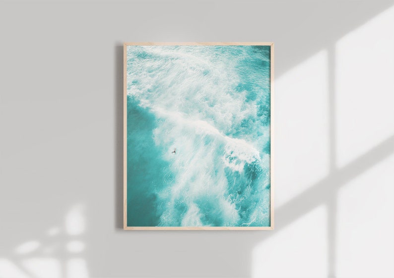 May include: An aerial view of a turquoise ocean with white waves crashing. A lone figure is seen surfing in the distance.