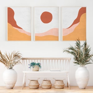 May include: Three framed abstract art prints with a minimalist design featuring orange, red, and white colors. The prints are hung on a white wall above a white bench with a potted plant and three woven baskets.