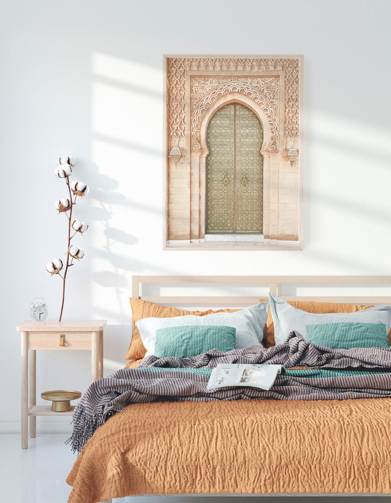May include: A bedroom with a bed with a brown and gray striped blanket and a teal pillow. A framed print of a carved archway with a door hangs on the wall above the bed.