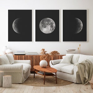 May include: Three black and white framed prints of the moon in different phases. The prints are hanging on a white wall above a light brown wooden cabinet.