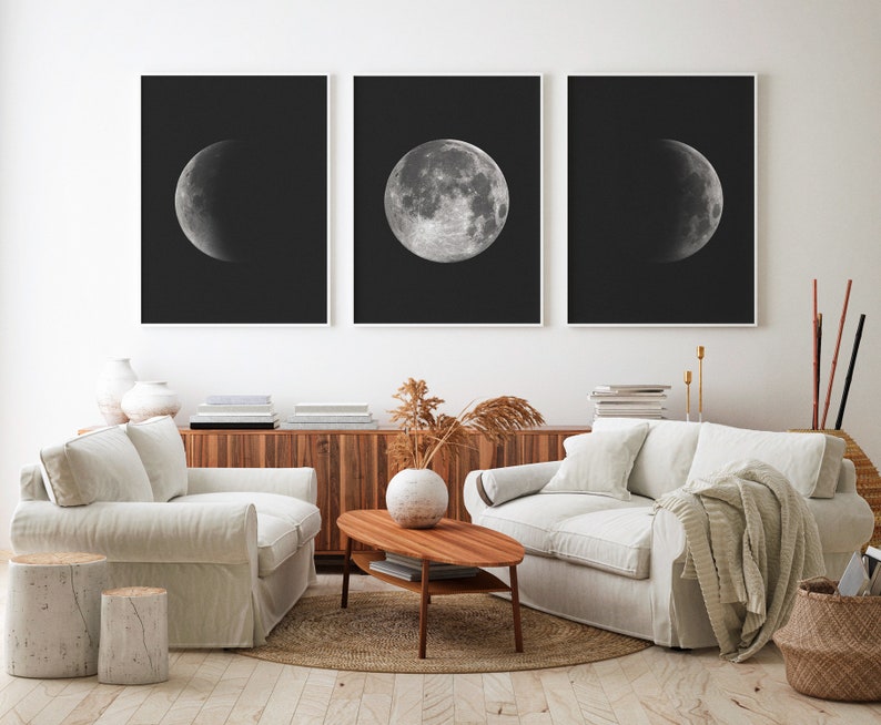 May include: Three black and white framed prints of the moon in different phases. The prints are hanging on a white wall above a light brown wooden cabinet.