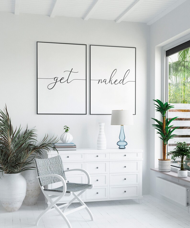 Puede incluir: Dos impresiones enmarcadas en negro con fondos blancos y texto negro. La impresi&oacute;n de la izquierda dice "get" y la impresi&oacute;n de la derecha dice "naked". Las impresiones est&aacute;n colgadas en una pared blanca sobre una c&oacute;moda blanca con cajones. Una silla blanca con un asiento tejido gris est&aacute; delante de la c&oacute;moda. Una planta en maceta est&aacute; a la izquierda de la c&oacute;moda y una l&aacute;mpara con una base de vidrio azul est&aacute; a la derecha de la c&oacute;moda.
