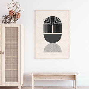 Pu&ograve; includere: Una stampa d'arte astratta geometrica in bianco e nero in una cornice di legno appesa a una parete bianca sopra una panca di legno. La stampa presenta un semicerchio nero, un arco nero con linee verticali e un semicerchio grigio.