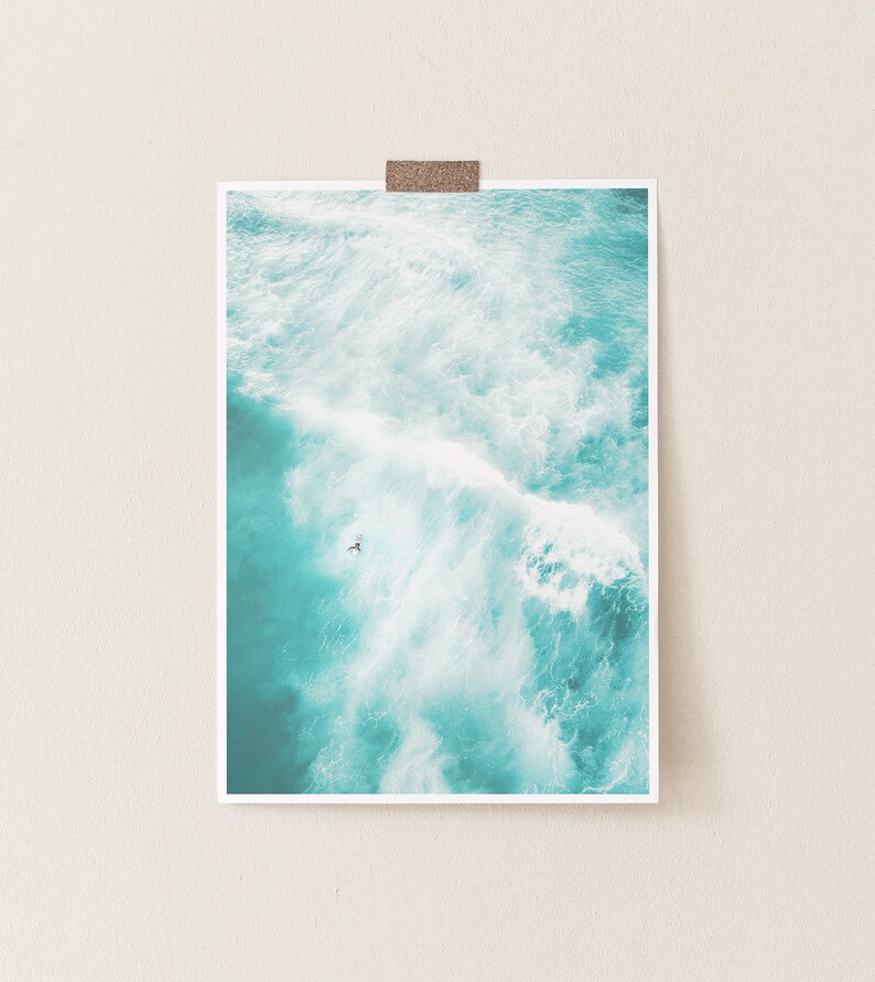 May include: An aerial view of a turquoise ocean with white foamy waves crashing. A single person is seen surfing in the water.