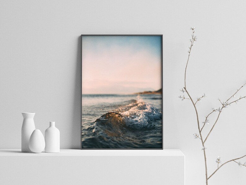 May include: A photograph of a wave breaking on a beach at sunset. The water is a deep blue and the sky is a soft pink and orange.