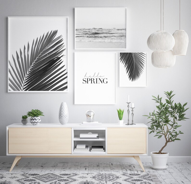 May include: A living room interior with a white media console and three black and white framed prints. The prints feature palm leaves and a beach scene. The text "hello spring" is written on one of the prints. The console is decorated with a vase, a plant, and a decorative object.