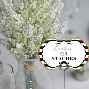 May include: Black and white striped table card with gold trim. The card has the text "lashes or staches" with a black mustache and eyelashes graphic.