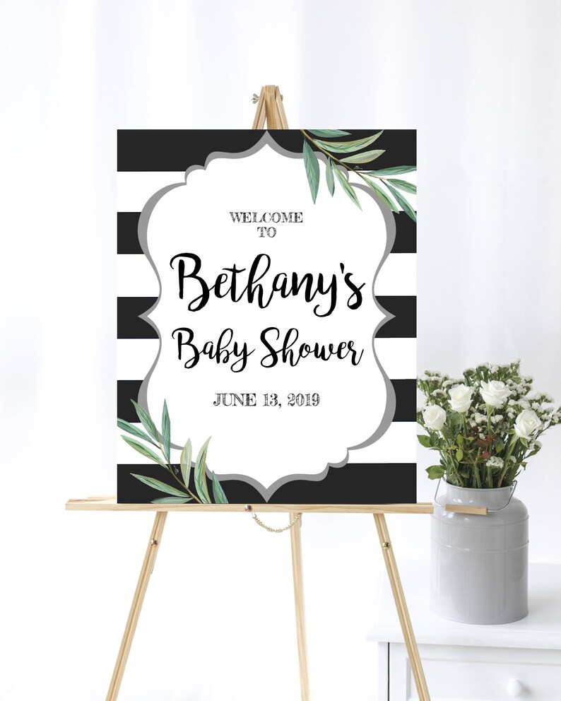 May include: Black and white striped welcome sign with a gray frame and green leaves. The sign reads "Welcome to Bethany's Baby Shower June 13, 2019".