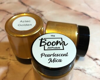 May include: Three jars of gold pearlescent mica pigment. The jar in the foreground has a white label that reads "Boom Art Products Pearlescent Mica 15g". The jar in the background has a white label that reads "Aztec Golden".