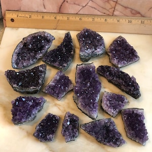 May include: A collection of 14 amethyst crystal clusters, each with a unique shape and size. The crystals are a deep purple color and have a natural, rough texture.