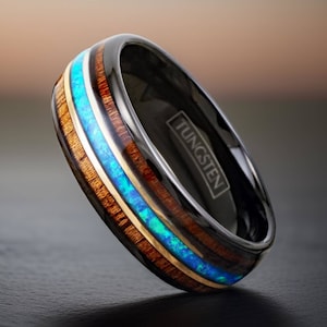 May include: Black tungsten ring with a wood inlay and a blue and green opal inlay. The ring is engraved with the word "TUNGSTEN".