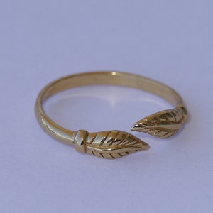 May include: A gold-toned ring with a leaf design on each side. The ring is open on one side and can be adjusted to fit different finger sizes.