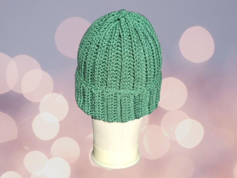 May include: A green crocheted beanie hat on a white mannequin head. The hat has a ribbed texture and a folded brim.