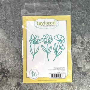 May include: A Taylored Expressions Simple Stems metal die set in a clear plastic package. The yellow card insert features three teal-colored flower outlines, the brand logo, and a barcode. The text reads Simple Stems, Item #1E2056, Made in China.