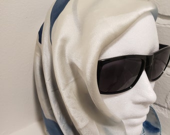 May include: A smooth, lustrous scarf featuring a light cream base with bold, flowing blue stripes. The scarf is draped over a white mannequin head that is wearing black, rectangular-framed sunglasses, creating a sleek and polished appearance.