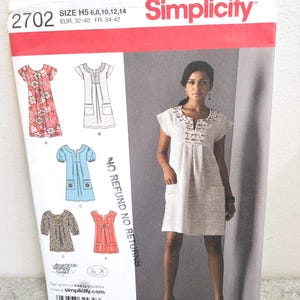 May include: Simplicity sewing pattern 2702. The pattern features a woman wearing a white dress with pockets. The pattern includes dress designs with various sleeve lengths and necklines. The size range is H5 6,8,10,12,14.