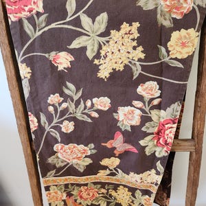 May include: A brown fabric tablecloth with a floral pattern featuring pink, yellow, and green flowers. The tablecloth has a border with a repeating pattern of small flowers.