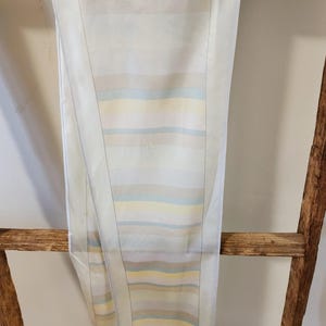 May include: A white silk scarf with a pattern of horizontal stripes in shades of beige, yellow, and blue.