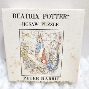 May include: A vintage jigsaw puzzle box featuring Beatrix Potter's Peter Rabbit. The box has a cream background with the title "BEATRIX POTTER JIGSAW PUZZLE" and an illustration of Peter Rabbit. The assembled size is approximately 18.4 x 18.4 cm.