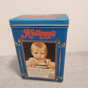 May include: A vintage Kellogg's Toasted Corn Flakes tin. The blue tin has the Kellogg's logo in red and a picture of a baby. The text on the tin reads "Always ready for Kellogg's Toasted Corn Flakes."