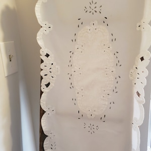 May include: White lace table runner with a scalloped edge and a delicate floral design. The runner is made of a lightweight fabric and has a subtle sheen.