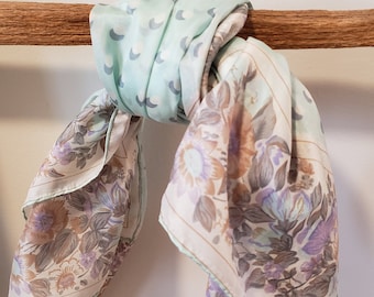 May include: A light blue and white patterned scarf with a floral design. The scarf is tied in a knot and draped over a wooden railing.