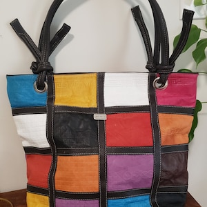 May include: A multi-coloured patchwork leather tote bag with black straps and a small silver tag that reads "Rock Bella".