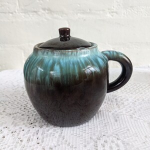 Op de afbeelding: Een bruine en turquoise geglazuurde keramische roomkan met een deksel en een handvat. De roomkan heeft een gemarmerde glazuur met turquoise en bruine strepen.