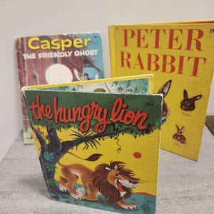 以下が含まれることがあります： カラフルな表紙のヴィンテージ子供向けの本の束。「Casper The Friendly Ghost」、「Peter Rabbit」、「The Hungry Lion」などのタイトル。ライオン、幽霊、ウサギのイラストが描かれています。