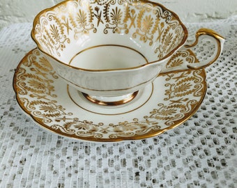 May include: A white teacup and saucer with a gold rim and intricate gold floral pattern.
