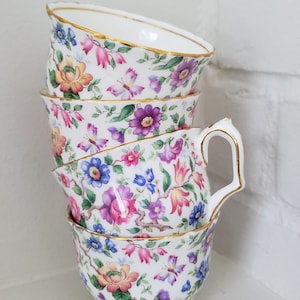 May include: A stack of four floral teacups with a gold rim. The cups are decorated with a variety of colourful flowers and butterflies.