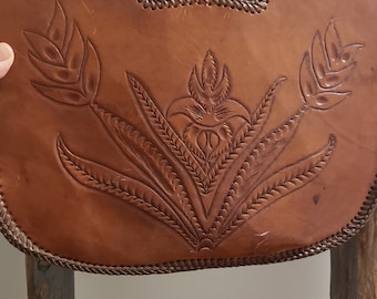 Peut inclure: Un sac à main en cuir marron avec un motif floral. Le sac a une poignée supérieure et une bordure tressée autour des bords.