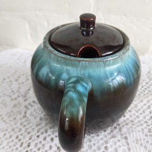 Op de afbeelding: Een bruine en blauwe geglazuurde keramische suikerpot met een deksel en een handvat. De kom heeft een gemarmerde glazuur met bruine en blauwe swirls.