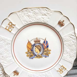 May include: White commemorative plate with a gold rim and embossed floral details. The plate features a central emblem with a portrait, flags, and text, and the letters "ER" in gold. The plate commemorates the Coronation of June 2, 1953.
