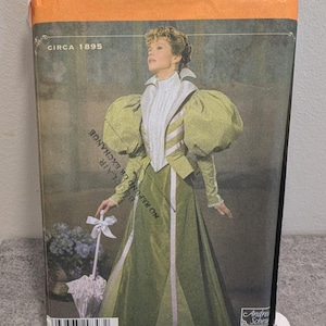 Peut inclure: Une pochette de patron de couture Simplicity pour un vêtement Circa 1895, montrant un modèle portant une veste vert clair à manches bouffantes et une jupe longue assortie, avec un chemisier blanc à col haut et une ombrelle blanche à nœud.