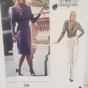 May include: Vogue American Designers sewing pattern featuring two designs by Bill Kaiserman. The pattern number is 2597. The first design is a purple dress with a high neck and long sleeves. The second design is a white blouse with long sleeves and white pants.