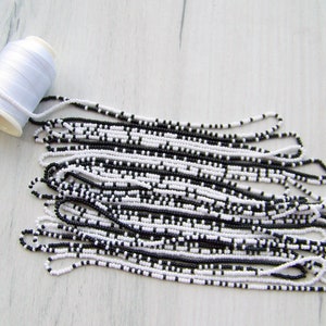 May include: A spool of white thread and a pile of black and white seed beads.