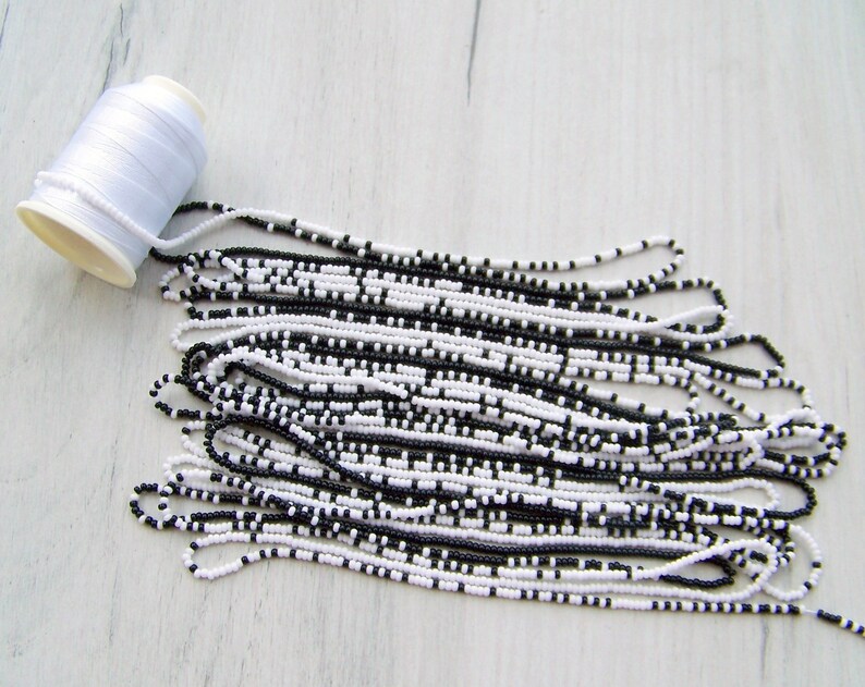 May include: A spool of white thread and a pile of black and white seed beads.