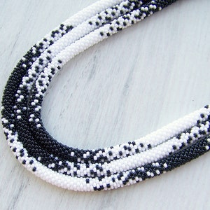 May include: A black and white beaded necklace with a graduated pattern. The necklace is made of small, round beads and is approximately 40 inches long.