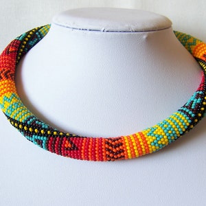 May include: A colorful beaded necklace with a geometric pattern in shades of turquoise, yellow, orange, and red. The necklace is made of small beads and is strung together in a tight, compact design.