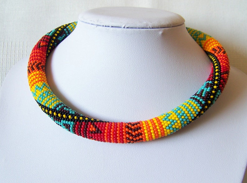 May include: A colorful beaded necklace with a geometric pattern in shades of turquoise, yellow, orange, and red. The necklace is made of small beads and is strung together in a tight, compact design.