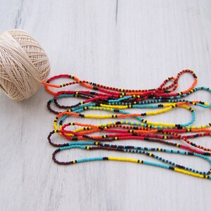 May include: A spool of beige thread with a long strand of colorful beads in shades of red, orange, yellow, blue, and brown.
