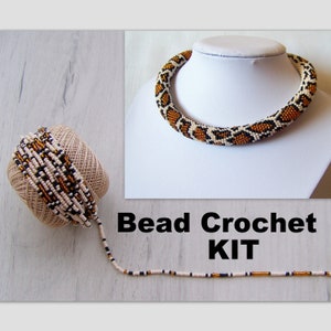 Könnte beinhalten: Ein Perlen-Häkel-Set zum Herstellen einer Halskette. Das Set enthält Perlen in Weiß, Schwarz und Gold sowie eine Spule Garn. Die fertige Halskette ist auf dem Bild zu sehen und hat ein Schlangenhautmuster.