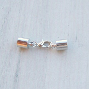 May include: Silver tone metal clasp with two cylindrical end caps. The clasp is designed for use with necklaces or bracelets.