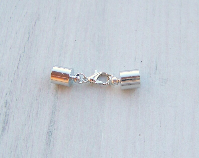 May include: Silver tone metal clasp with two cylindrical end caps. The clasp is designed for use with necklaces or bracelets.